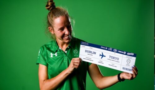 female holding a large boarding pass in front of a green background