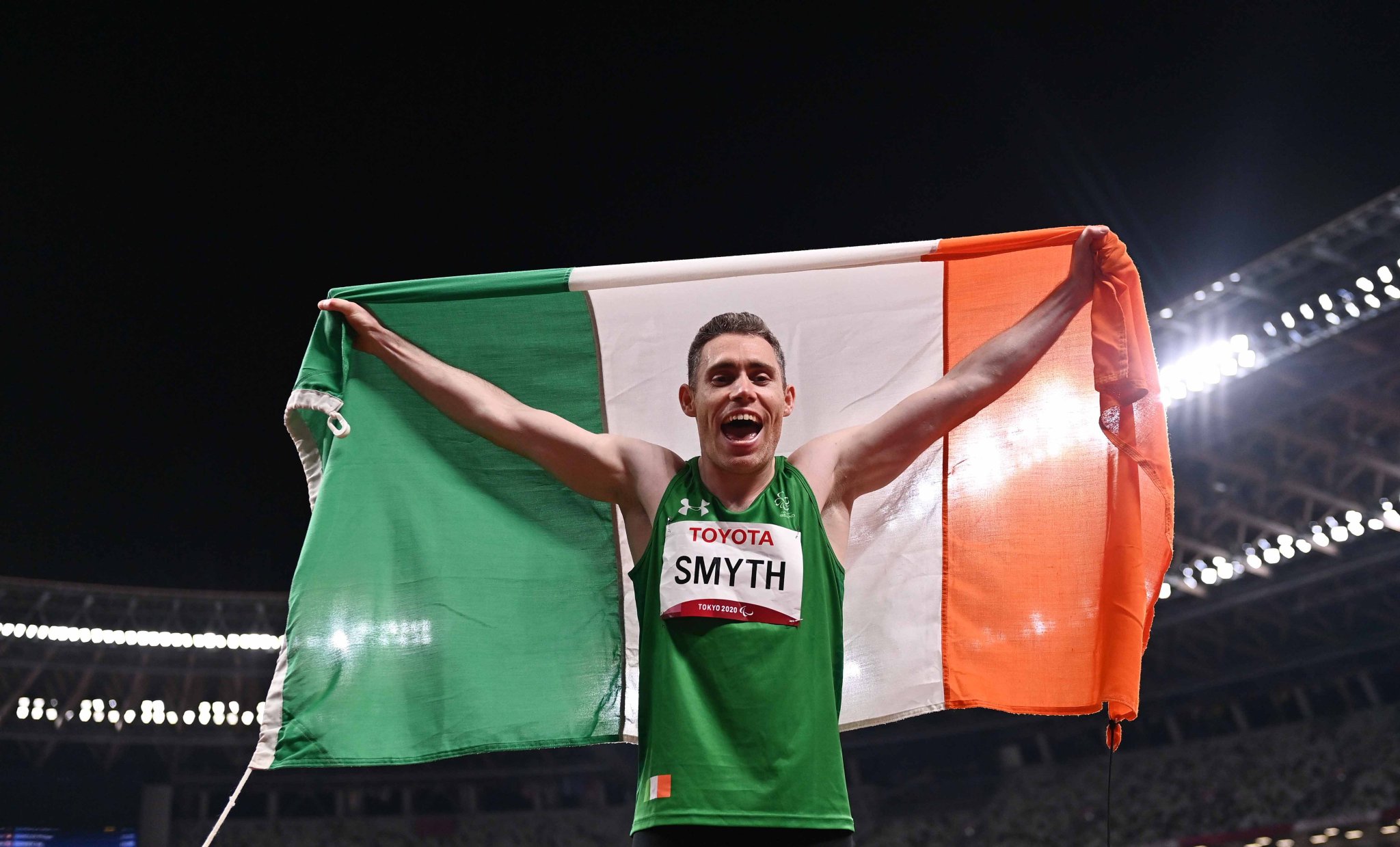 male Irish paralympic athlete holding an Irish flag behind his head