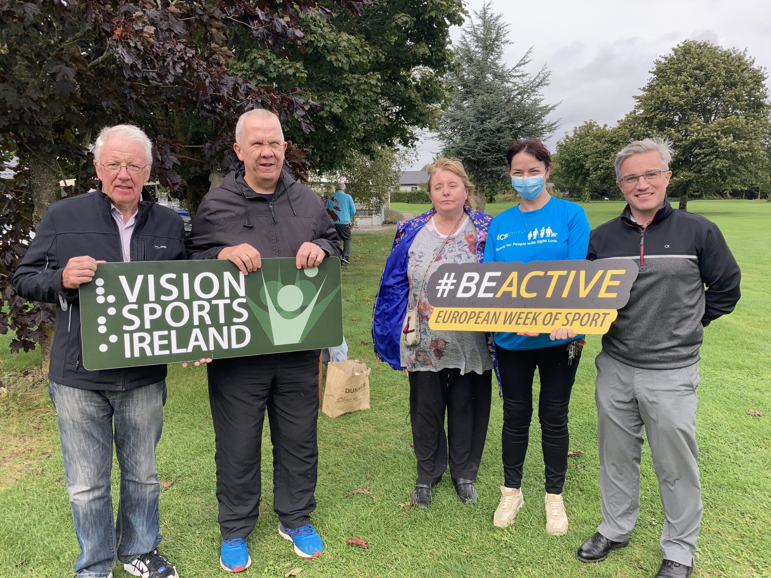 A group of men and women holding a Vision Sports Ireland sign and a #BeActive sign while standing on a golf course