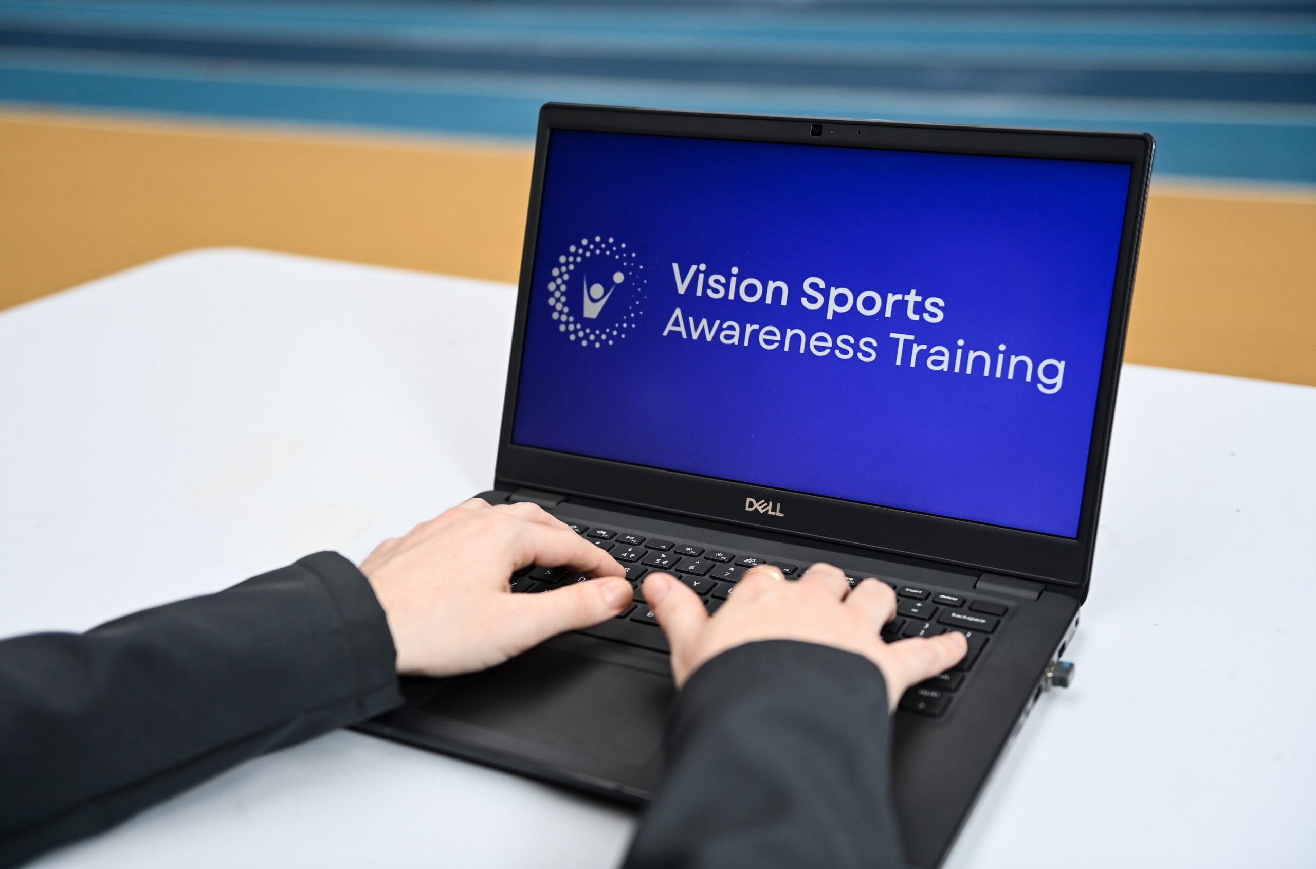 A person's hands typing on a laptop keyboard. The screen of the laptop has a blue background with the words Vision Sports Awareness Training written in white font