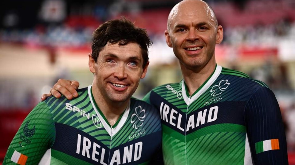 Martin and Eamonn smiling at the camera in green and black team Ireland cycling suits