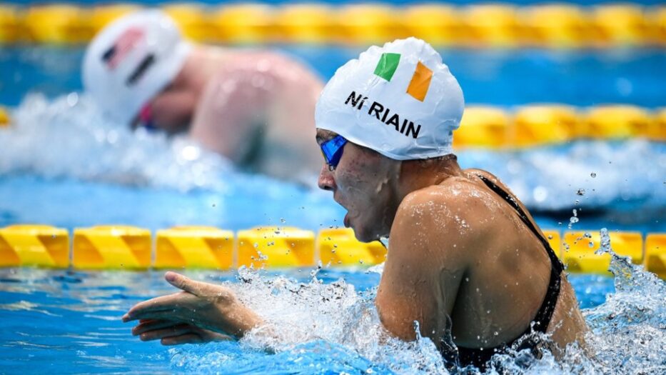 Photo of Roisin racing breaststroke in the pool wearing a white swimming cap with the Irish flag on it