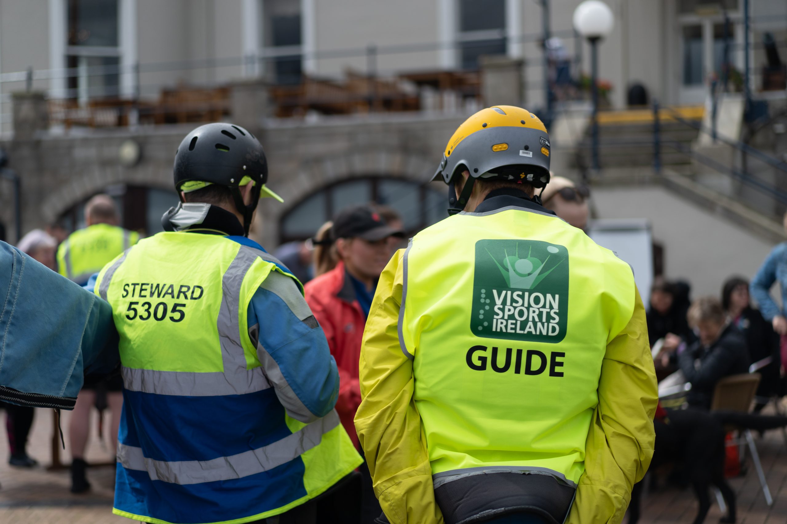 a photo from behind of two guides, both are wearing hi vis vests. one has the word guide and the vsi logo on it