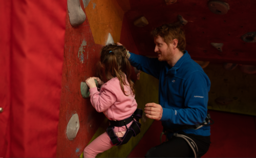 Young female participant on a climbing wall supported by her instructor