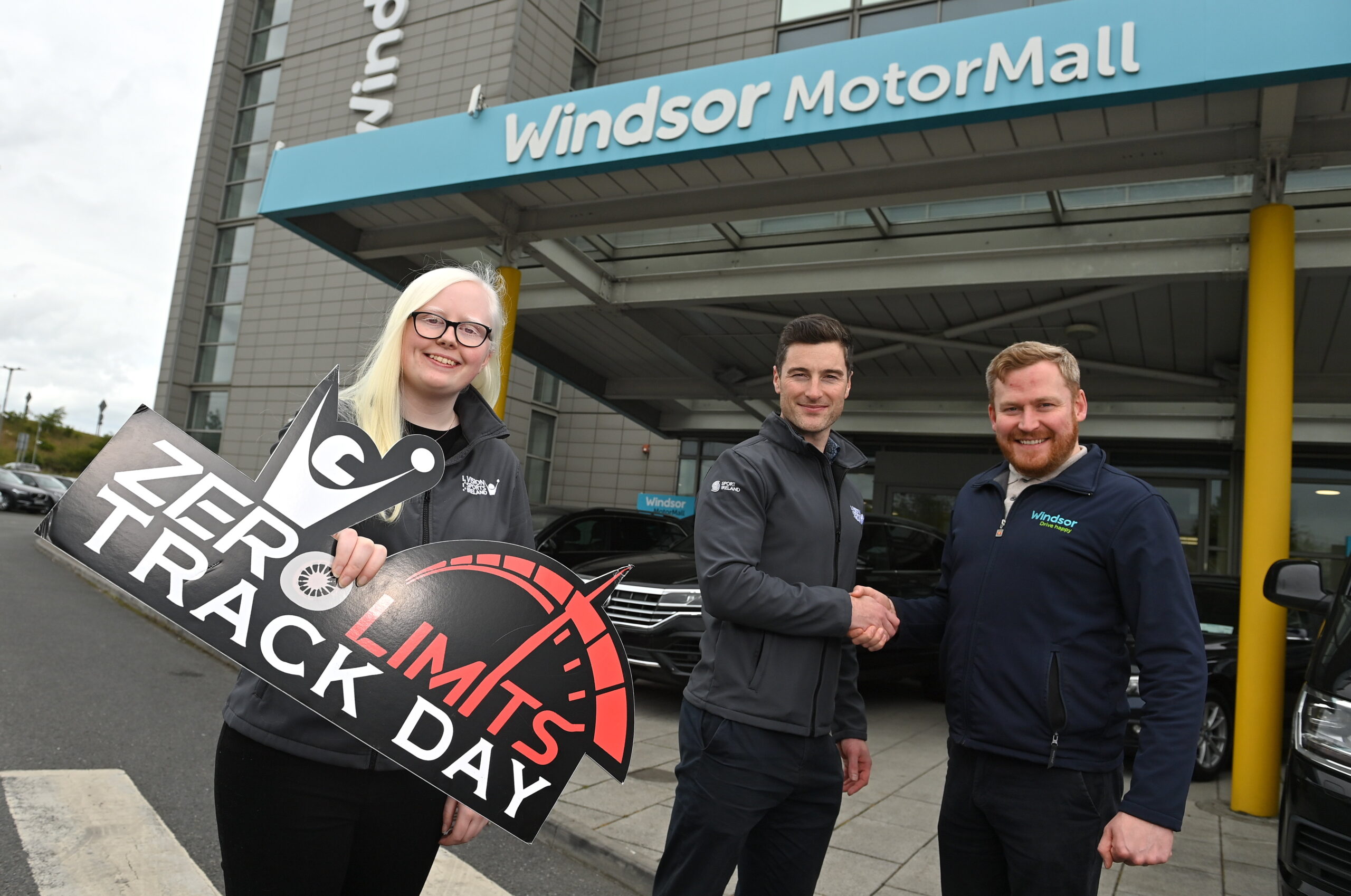 Zero Limits launch photo of 3 people, 2 shaking hands and 1 holding a zero limits logo sign outside Windsor Motor Group