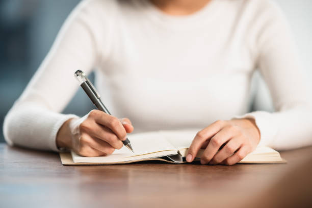 Image of a female writing on a notebook wearing a white top