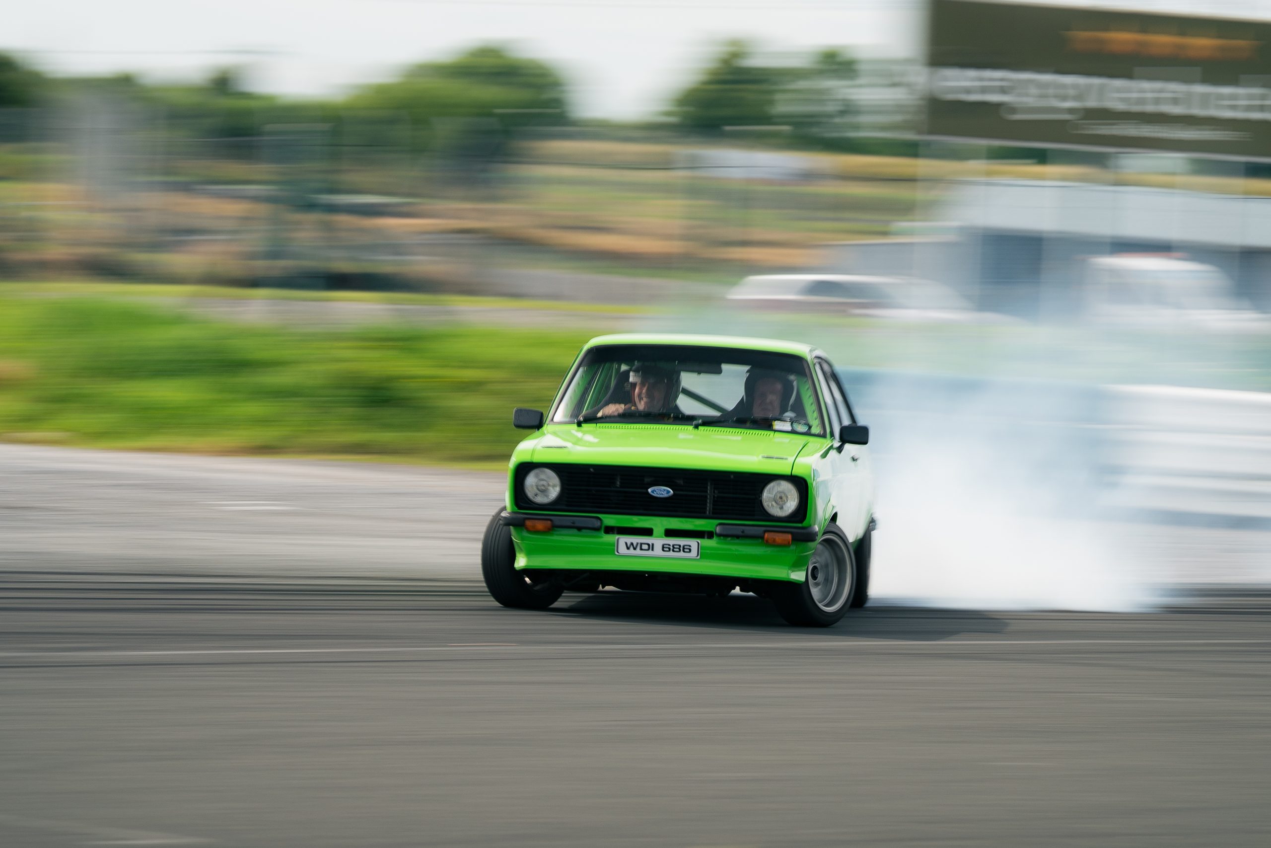 Image of a green ford escort drifting sideway with smoke coming from the back wheels