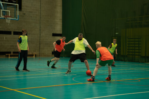 Photo of a group of four men in yellow and orange high vis vests playing football