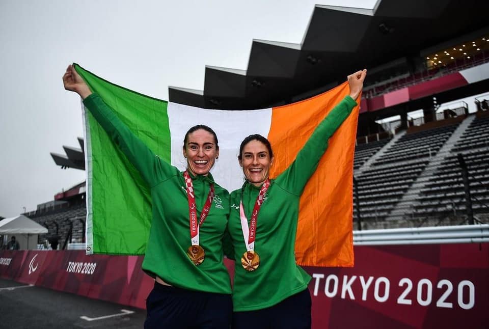 Photo of Katie George and Eve on the podium with gold medals and an Irish flag
