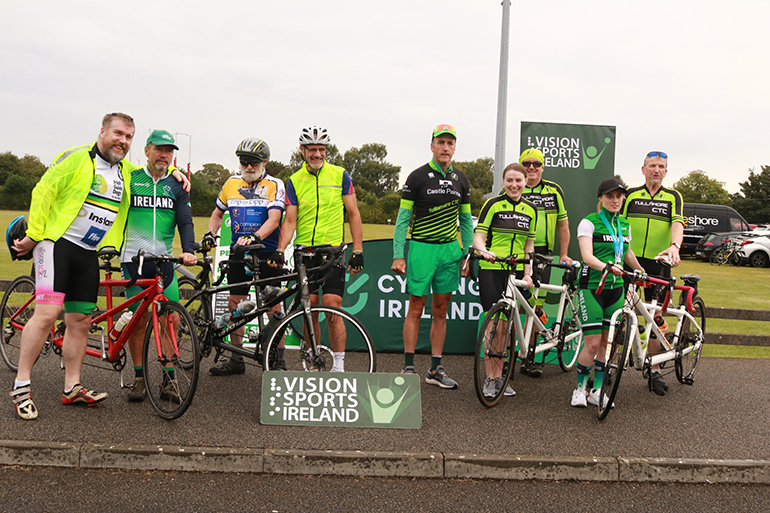 Group of participants and volunteers with tandem bikes and branding.