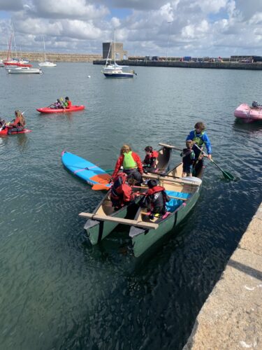 Photo if kids in bright coloured life jackets on a boar with a stand up paddle board