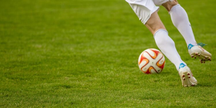 footballers feet controlling a white and orange ball