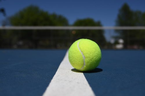 yellow tennis ball sitting on a blue court with a white vertical line up the centre,