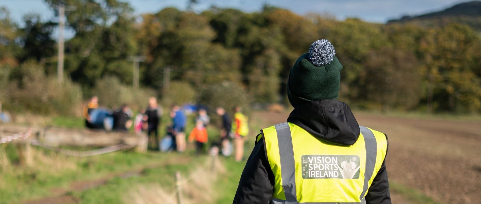 Image of a persons back wearing a vision sports ireland hi vis jacket looking towards a group partaking in activity