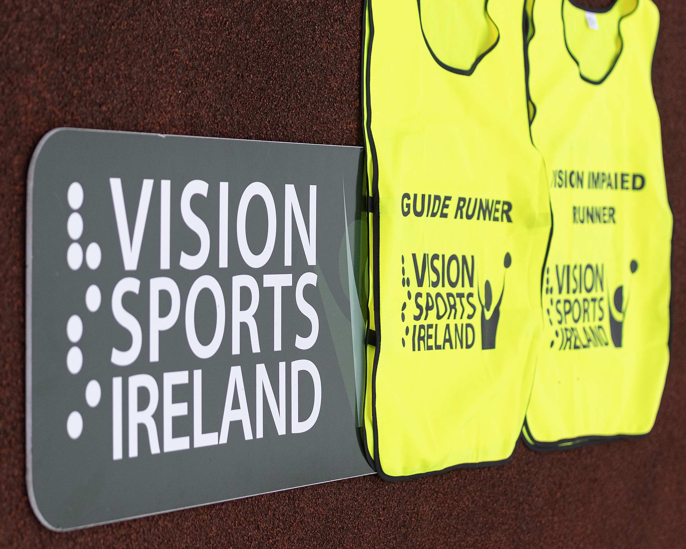 A vision Sports Ireland sign on the ground with a guide runner and vision impaired runner yellow bib on top of it.