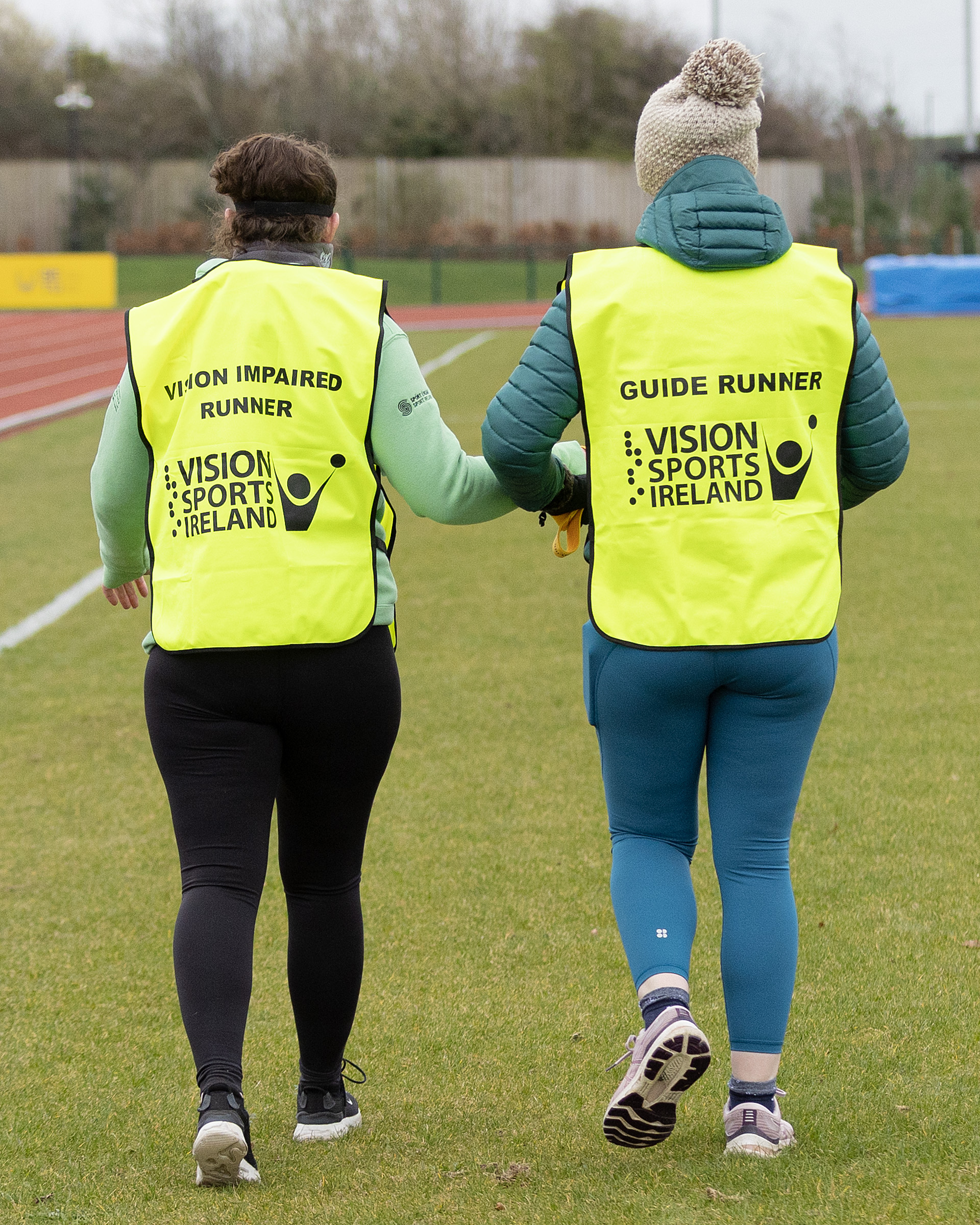Two participants in the Guide Running Workshop. One is wearing a VI runner yellow bib and the other participant is wearing a guide runner yellow bib