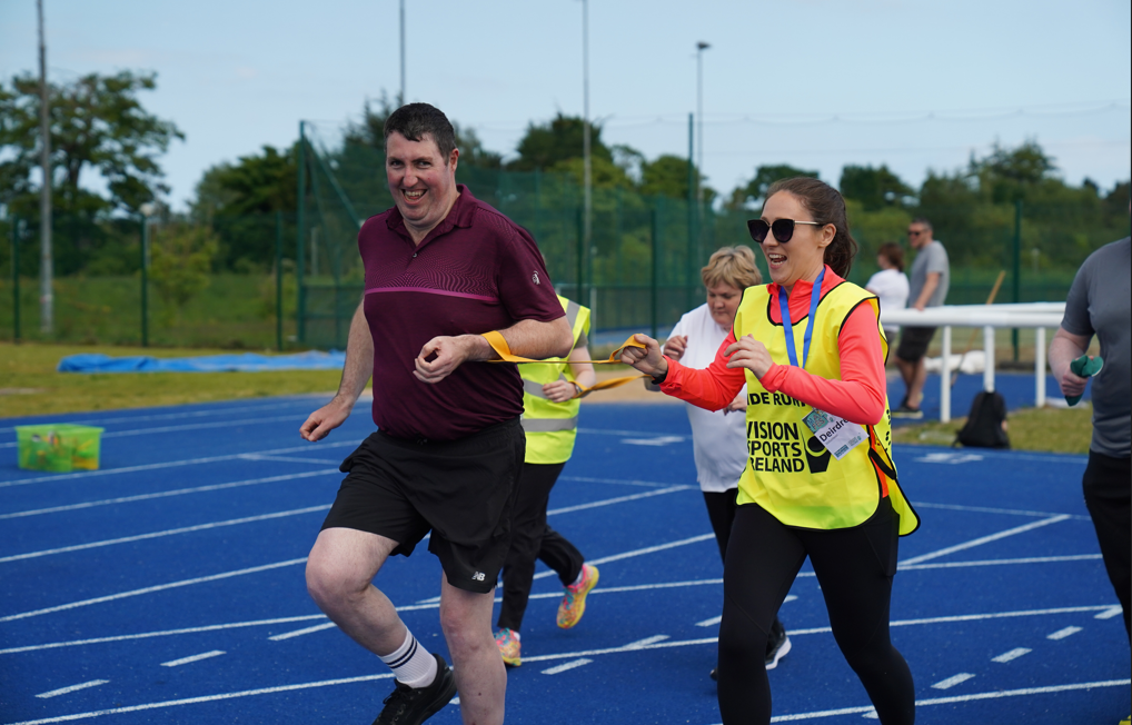 Athlete John and Guide Deirdre smile as they are running on the blue athletics track.