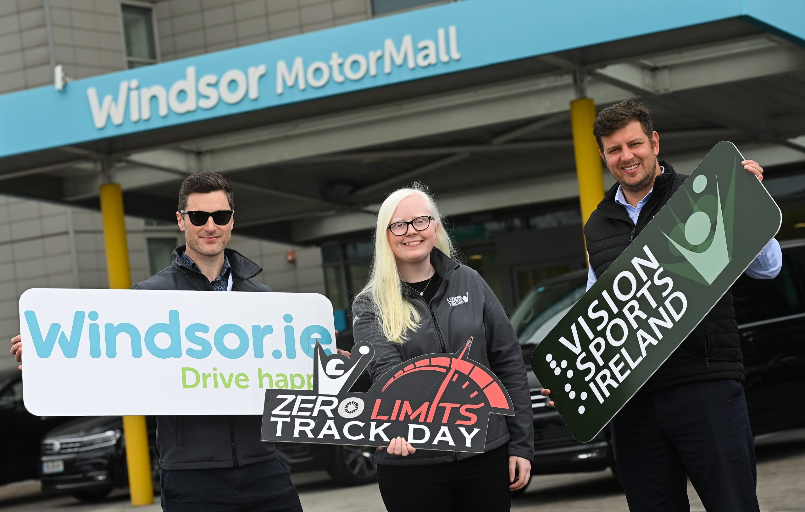 3 people post for a photo outside windsor motor group holding, windsor, VSI and zero limits logo signs