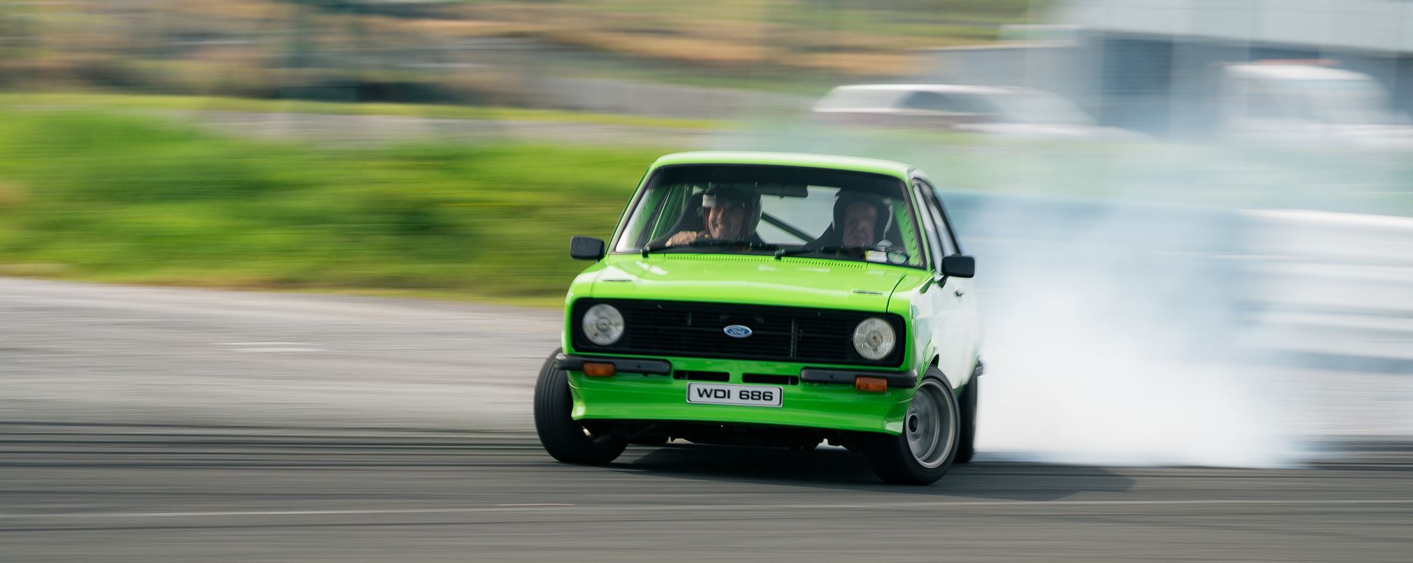 A green MKII escort drifting on a track with tyre smoke