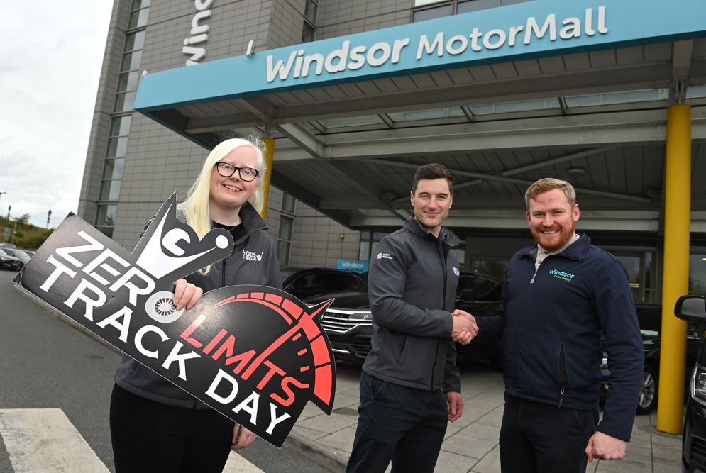 4 people post for a photo outside windsor motor group, 2 shake hands and the other holds a zero limits logo sign