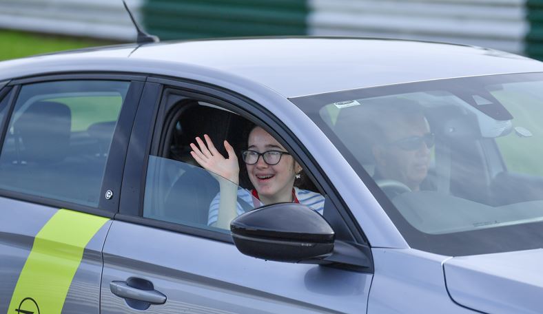 a young girl who is smiling waves from the drivers seat of a car