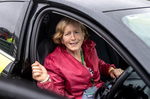 A woman sitting behind the wheel of a car and smiling to the camera.