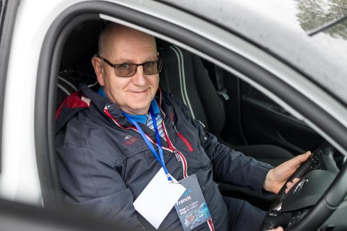 A man sits behind the wheel of a car and smiles at the camera.