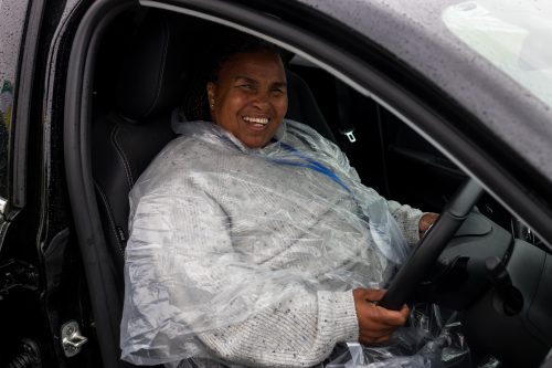 A woman sits behind the wheel of a car and smiles at the camera.