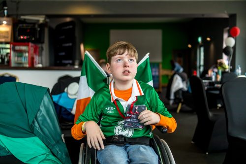 A participant dressed in an Ireland jersey with Ireland flags behind him watches the Women's World Cup game at #ZeroLimits23