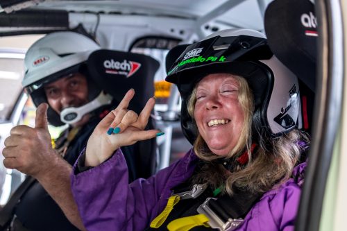 A rally driver and female participant smile and wave to the camera before heading out on track