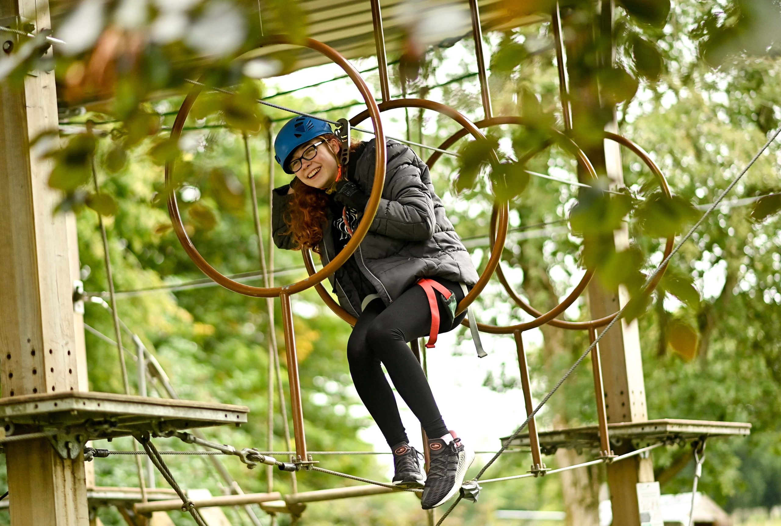 A girl goes through rings in an obstacle course in the woods. She is attached by a harness and is laughing