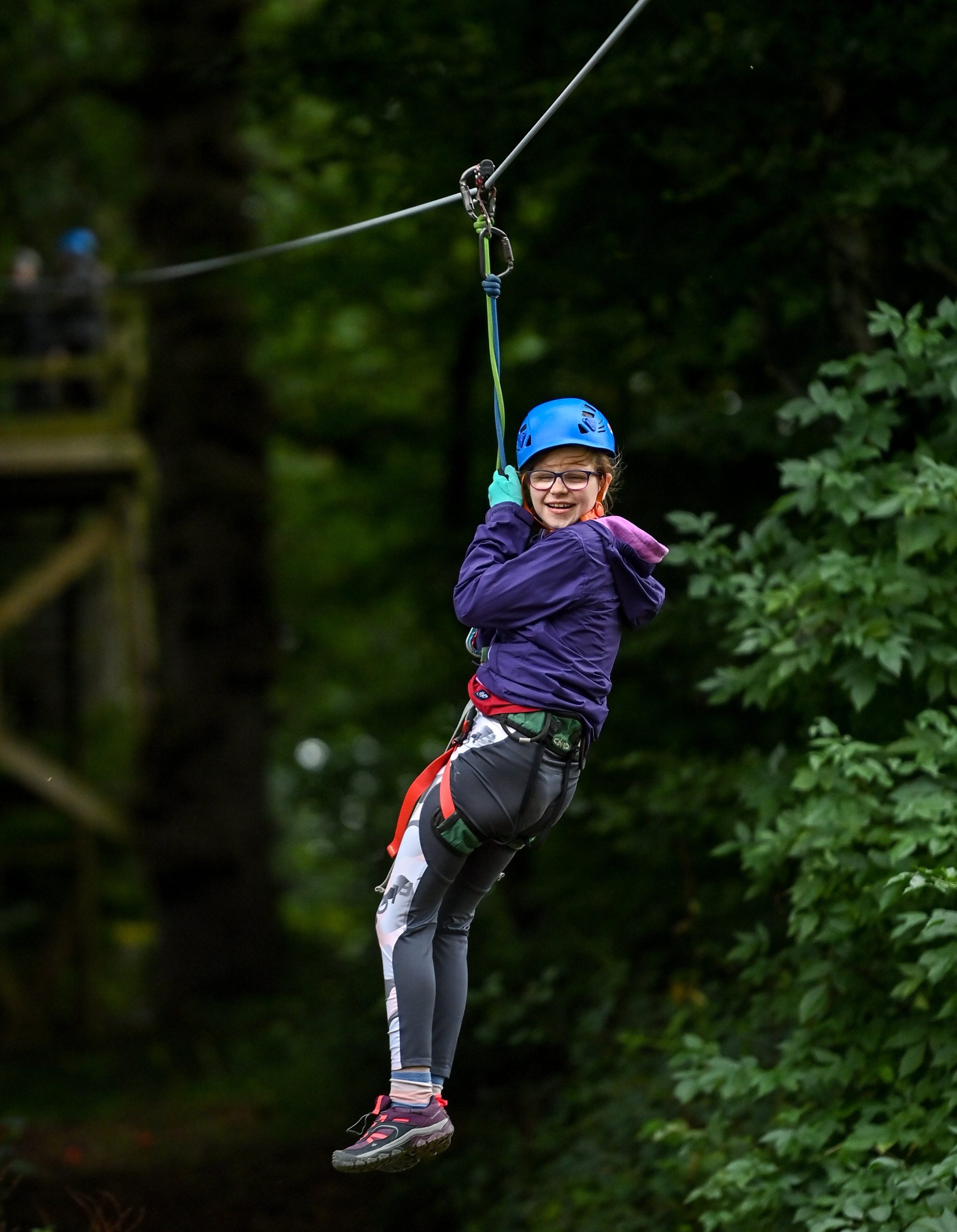 A girl on a zipline going through a forest smiles at the camera