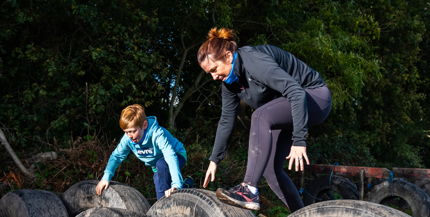 Image of a mother and son climbing over tyres at an adventure course
