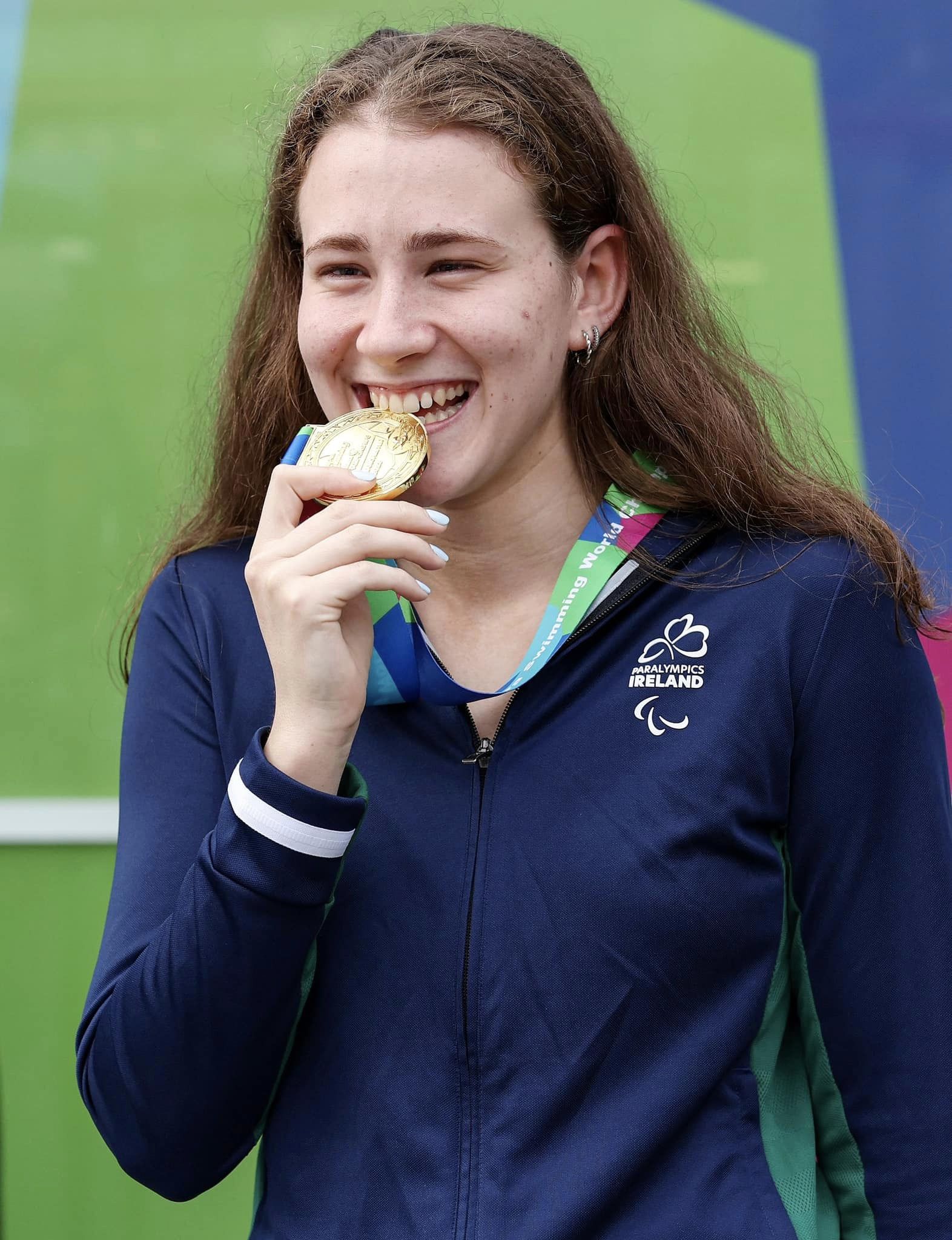 Roisin NI Riain bites into a gold medal while smiling at the camera
