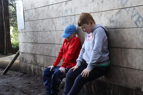 2 young boys crouching with their backs against a wall