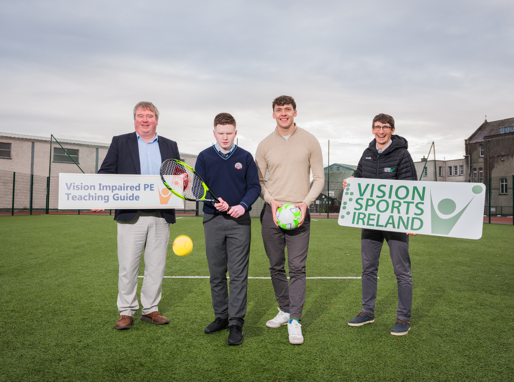 Senator Martin Conway, student Michael O Brien, Kerry footballer David Clifford and Padraig Healy from Vision Sports Ireland stand holding signs a football and a tennis racket to launch the Vision Impaired PE Teaching Guide.