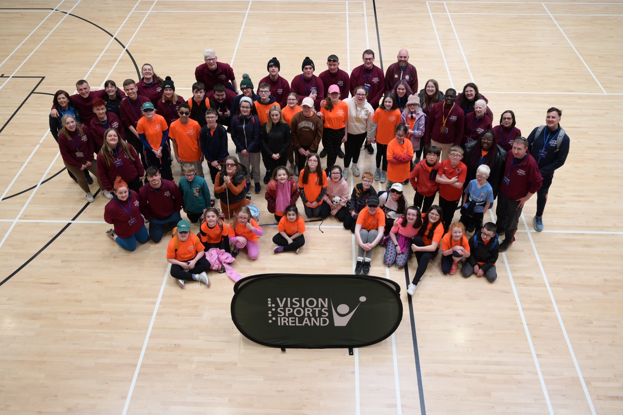 A group photo of all camp volunteers and participants taken in a sports hall from above