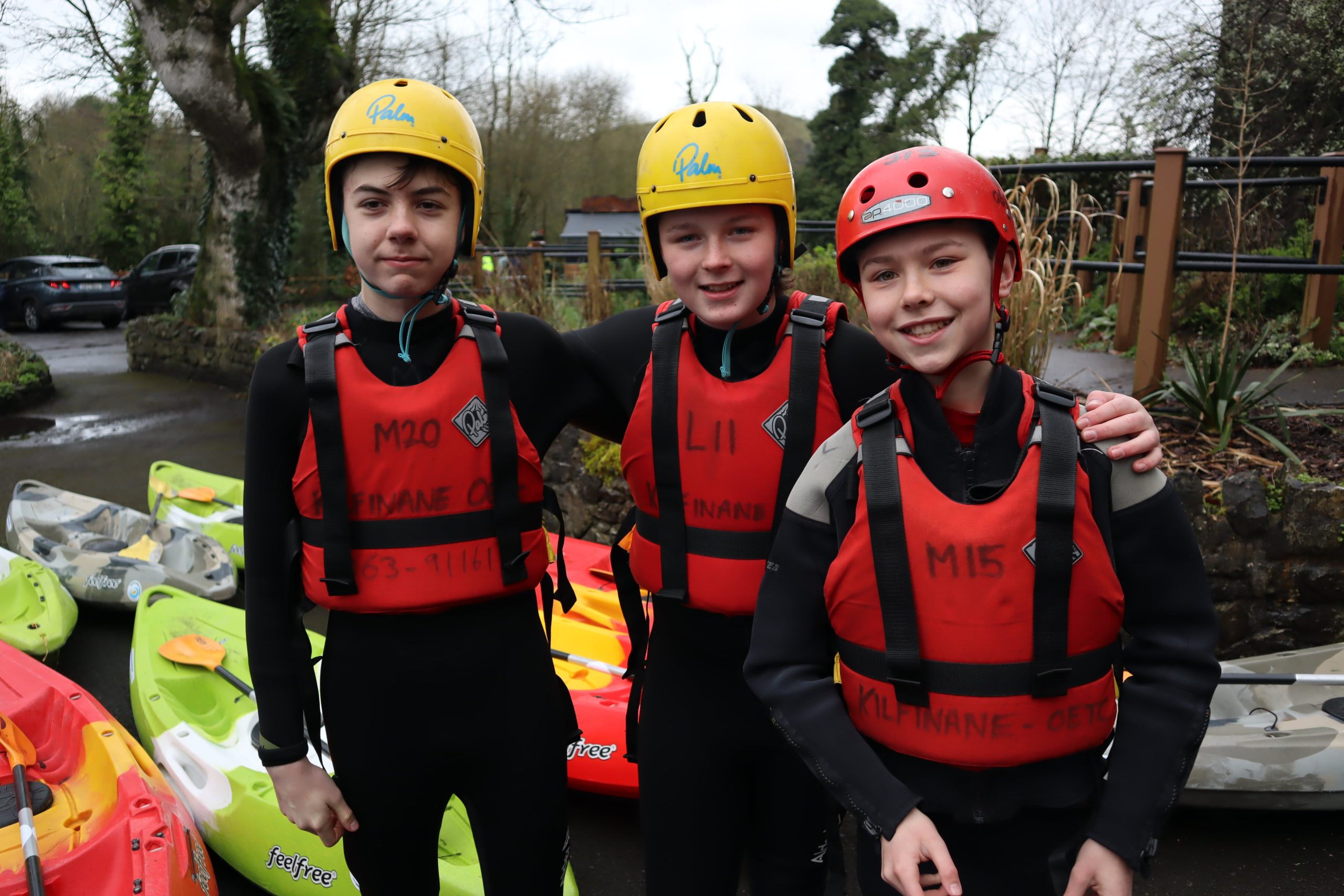 3 boys wearing lifejacket and helmets standing for a photo before kayaking