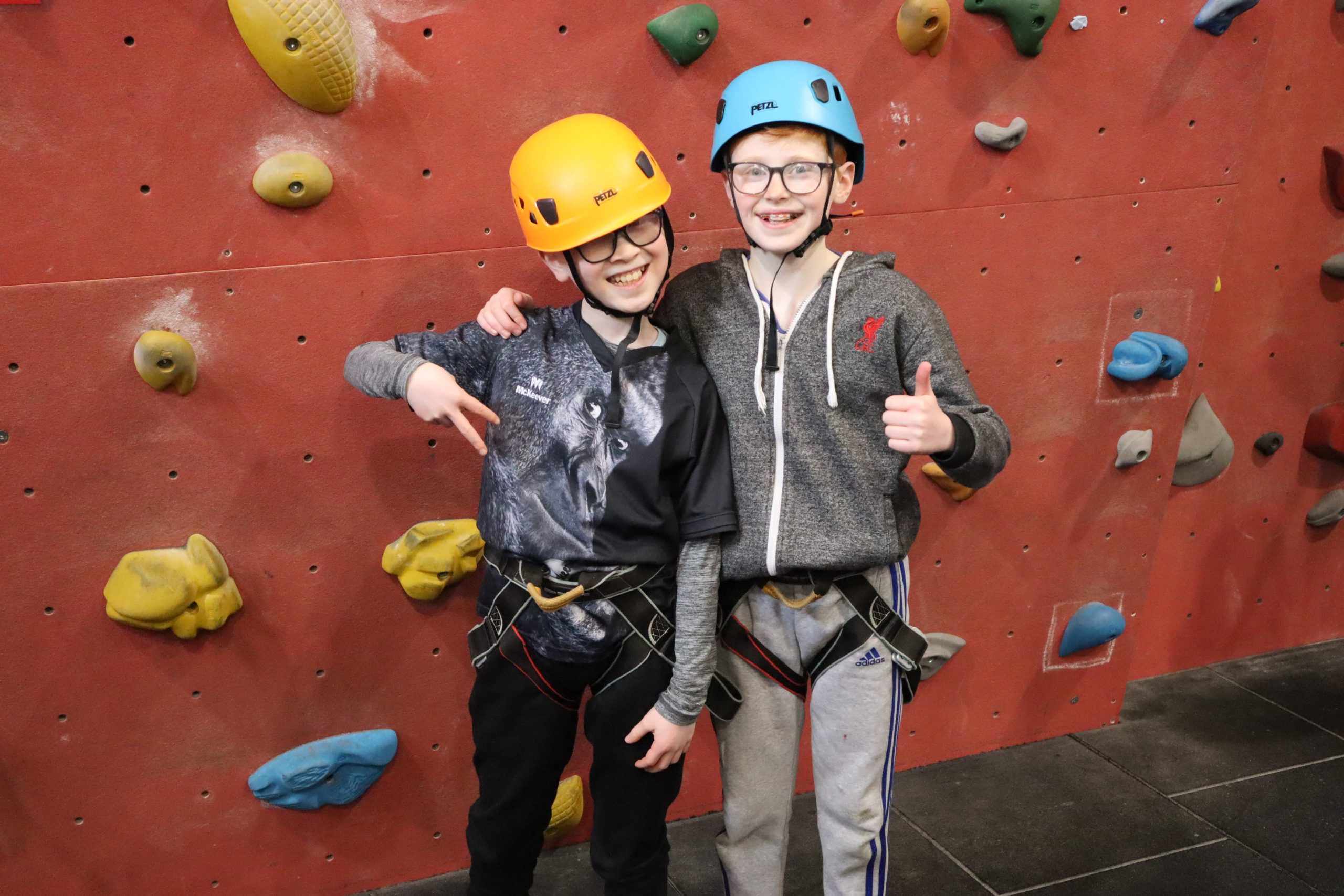 2 boys pose for a photo in front of a rock climbing wall