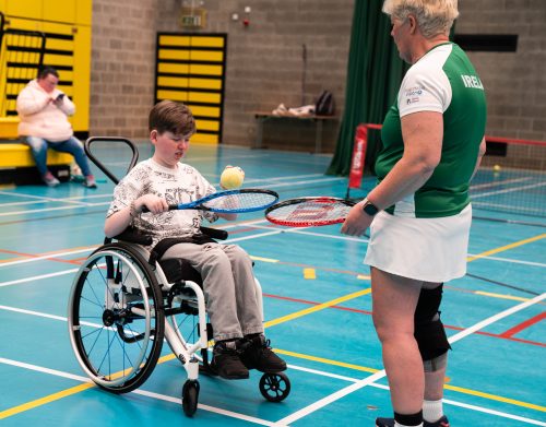 a young participant receives tennis coaching from a member of the Irish Blind/VI tennis team
